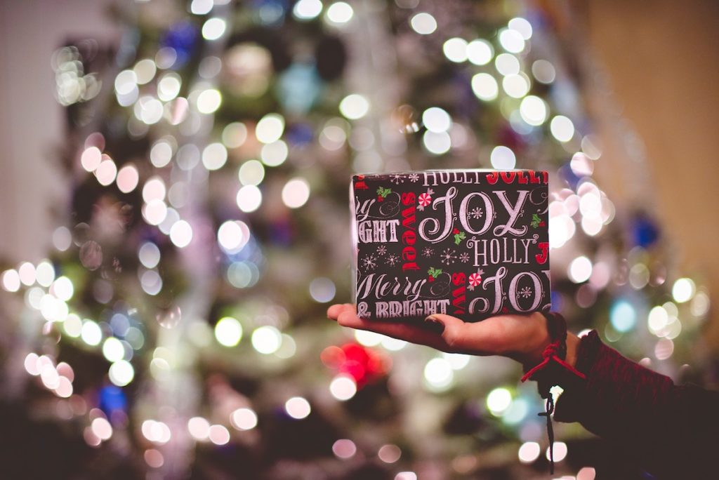 Hand holding one present in front of Christmas tree: the one-gift rule for the holidays limits toddler gift overload!